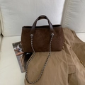 Dettaglio borsa tote in pelle scamosciata marrone con manici e catena su divano bianco - Marrone