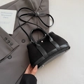 Minimalist black leather tote bag with dual handles and crossbody strap on suit jacket - Black