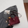 Burgundy bucket bag with suede texture, silver clasp, and decorative charms on a gray blazer - Wine Red With Pendant