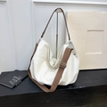 Detail der cremeweißen Canvas-Hobo-Tasche mit braunem Webriemen auf dunklem Holztisch - Weiß