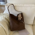 Detail der dunkelbraunen Wildleder-Beuteltasche mit Plüschbär-Anhänger auf weißem Sofa - Kaffeebraun (Mit Anhänger)