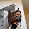 Détail d'un sac seau marron avec motif litchi, fermoir rotatif et charm de chiot en peluche - Café avec Pendentif