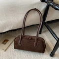 Detailaufnahme der dunkelbraunen Wildleder-Zylindertasche mit weißen Nähten auf Teppich - Braun