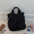 Detail of black canvas tote bag showing large front pockets and drawstring toggle side - Black