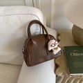 Detail einer braunen Wildleder-Bowlingtasche mit einem Plüschhund-Anhänger am Griff - Braun mit Anhänger