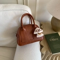 Detail der braunen Retro-Wildleder-Bowlingtasche mit Logo und süßem Hundeanhänger - Gelbbraun Mit Anhänger