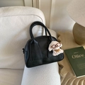 Detail einer schwarzen Bowling-Tasche aus Leder mit Logo-Prägung und Plüsch-Hundeanhänger - Schwarz Mit Anhänger