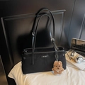 Close-up of black shoulder bag with metal logo, drawstring detail and a cute plush dog charm - Suede Look With Charm / Black