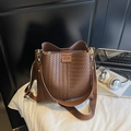Gros plan d'un sac seau tressé marron caramel avec bandoulière large et détail logo - Carreaux marron