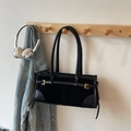 Dettaglio di una borsa baguette nera vintage con fibbie dorate appesa a un gancio di legno - Nero