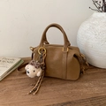 Detalle de un bolso Boston de cuero marrón en una mesa de madera con un amuleto de oso - Marrón con Colgante