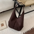 Detail view of deep brown suede hobo bag hanging on a woven chair in a warm setting - Brown