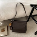 Detail view of a dark brown bucket bag with smooth texture and baseball charm on a rug - Coffee With Pendant