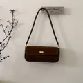 Detail van een bruine suède okseltas met gouden metalen gesp en slanke schouderriem - Bruin