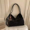 Detailopname van zwarte suède hobo-tas met bronzen oogjes en pluchen berenhanger - Zwart Met Hanger
