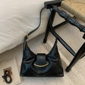 Dettaglio borsa a mezzaluna in pelle nera con fibbia dorata su un tappeto bianco puro - Nero