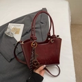 Detail view of deep red leather bucket bag featuring a woven strap and embossed logo texture - Wine Red With Pendant