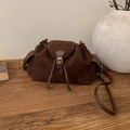 Detail view of brown suede bucket bag with leather trim and gold buckle on wooden surface - Brown