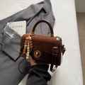 Detalle de bolso de mano marrón con cierre de giro dorado y colgante de cuentas de colores - Con Colgante / Burdeos