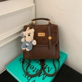 Minimochila marrón de ante con un colgante de oso sobre un libro azul decorativo - Café Con Colgante