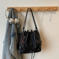 Chic black drawstring bucket bag with woven ring charm hanging on a wooden rack - Black (With Charm)