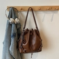 Detail of coffee brown matte bucket bag featuring drawstring closure and woven charm - Brown (With Pendant)