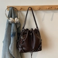 Detail of vintage brown bucket bag with drawstring closure and a pretzel charm on wood - Coffee (With Pendant)
