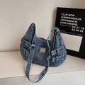 Detailopname van blauwe denim crossbodytas met zijgespen en metalen plaatje op textuurtafel - Blauw