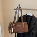 Detail der dunkelbraunen Wildleder-Baguette-Tasche mit goldenem Metalllogo und Perlenanhänger - Mit Anhänger / Kaffeebraun