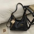 Detail of black leather tote bag featuring antique bronze buckle and bear charm accessory - Black With Pendant