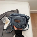 Close-up of vintage blue denim crossbody bag featuring dual zippers and brown leather logo patch - Blue