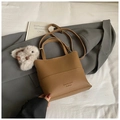 Close-up of brown textured leather bucket bag with a white plush rabbit pendant and handle - Brown with Pendant