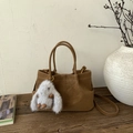 Detailed close-up of brown suede bucket bag with a gray plush bunny charm on wooden table - Brown with Pendant