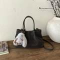 Detail of dark brown suede bucket bag with a cute white plush bunny charm on wooden table - Ebony with Pendant