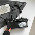 Primer plano de un bolso tote de charol negro con hebillas plateadas sobre fondo gris sobrio - Negro