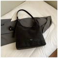 Détail du sac hobo en cuir mat noir avec logo posé sur des vêtements et de la literie - Noir