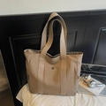 Detailed close-up of khaki nylon tote bag on white bed with art book and headphones - Khaki
