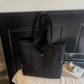 Detail shot of black canvas tote bag showing the side brand label and metal buckle fastener - Black