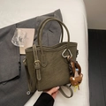 Detalle de bolso tote verde oliva con textura de lichi y colgante de oso en ropa de cama blanca - Con Colgante / Verde
