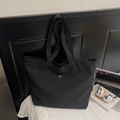 Détail du sac cabas en nylon noir avec logo CM en métal dans un bureau minimaliste - Noir