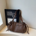 Detail view of brown leather tote bag with drawstring side and metal logo plaque - Coffee
