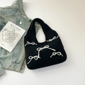 Detail of black knitted tote bag featuring a decorative white pearl bow and soft texture - Black