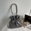Quilted silver drawstring shoulder bag shown with lifestyle items on a white desk - Gray