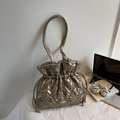 Close-up of champagne gold quilted puffer bag with drawstring on a minimalist desk - Gold