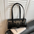 Close-up of black leather underarm bag with large silver buckle on black sofa - Black