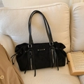 Detalle de bolso tote de ante negro con borlas plateadas y placa metálica en un sofá - Negro