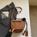 Dettaglio di una borsa a secchiello in camoscio marrone con frange e pompon su un letto - Marrone Cammello Caldo Con Ciondolo