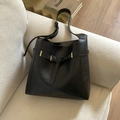 Close-up of black leather tote bag with gold buckle on a sofa in a modern home setting - Black