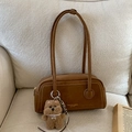 Detalle del bolso de ante marrón con colgante de osito de peluche en un sofá suave - Marrón con Colgante