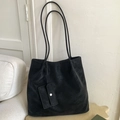 Detail of minimalist black suede tote bag with small attached pouch on a white sofa - Black